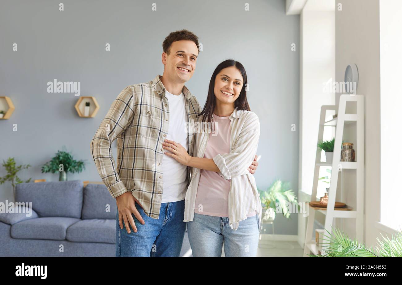 Portrait de jeune couple marié heureux debout dans le salon à la maison et serrant. Banque D'Images