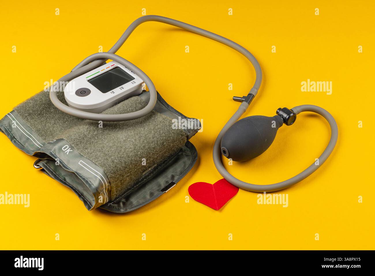 Élégant tensiomètre repose sur une surface jaune vif, accompagné d'une découpe de coeur rouge, symbolisant la santé et le bien-être dans un s minimaliste Banque D'Images