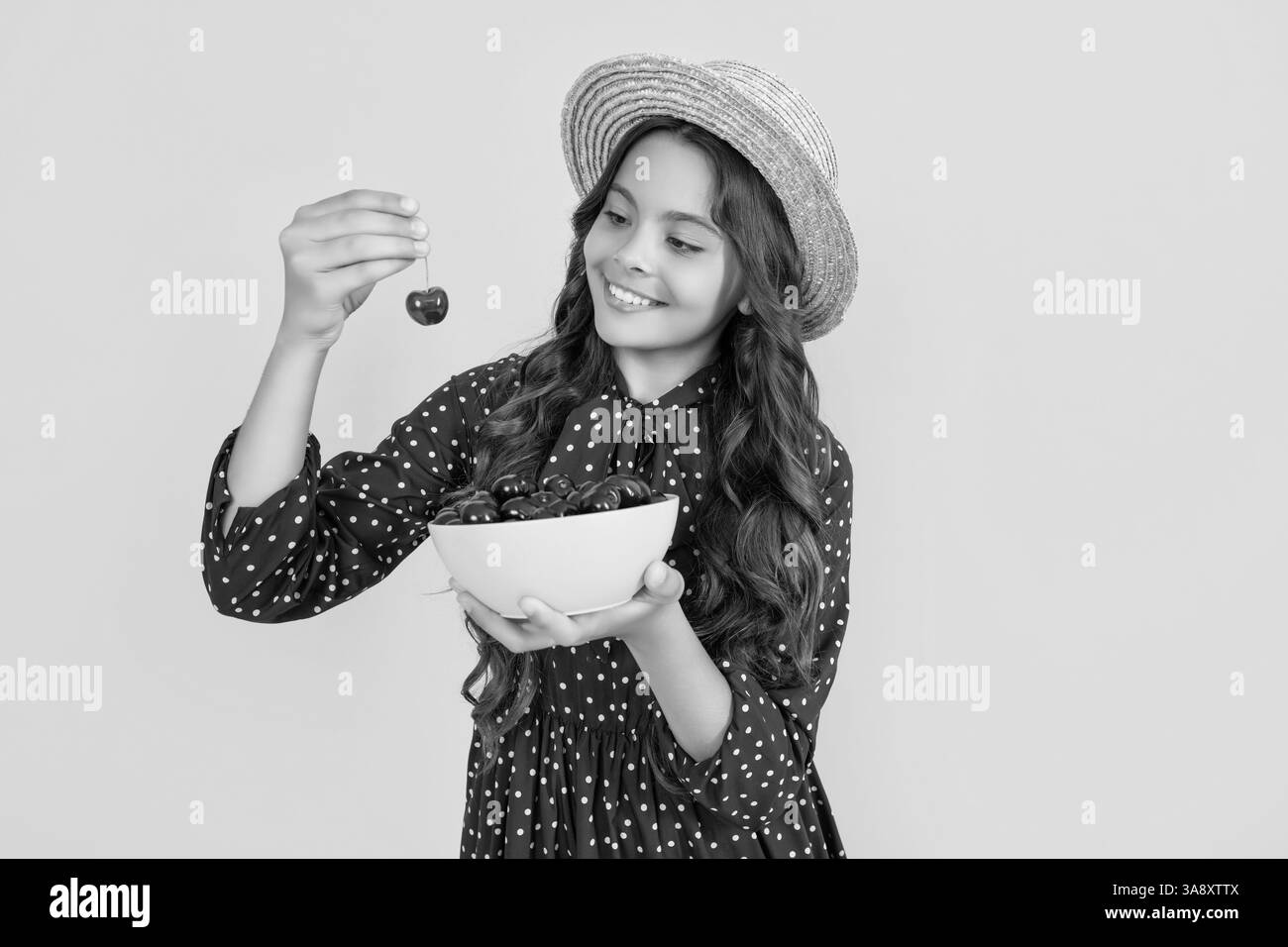 un adolescent heureux mange un bol de cerise sur fond jaune Banque D'Images