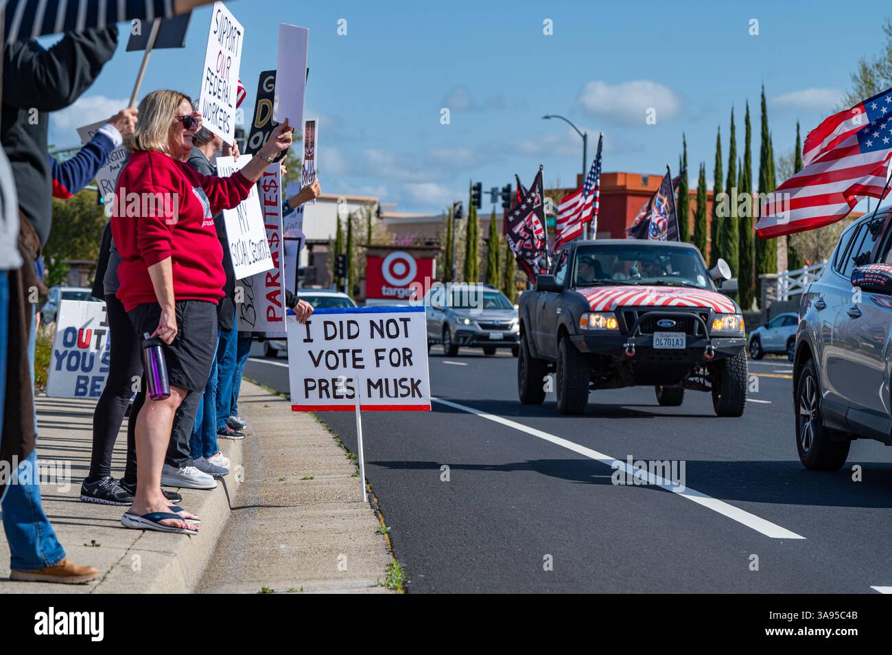 Les partisans de DOGE/MAGA avec des drapeaux passent devant les manifestants en face de la concession Tesla. Les manifestants de Tesla Takedown et Takeback ont assisté à l'événement. Banque D'Images