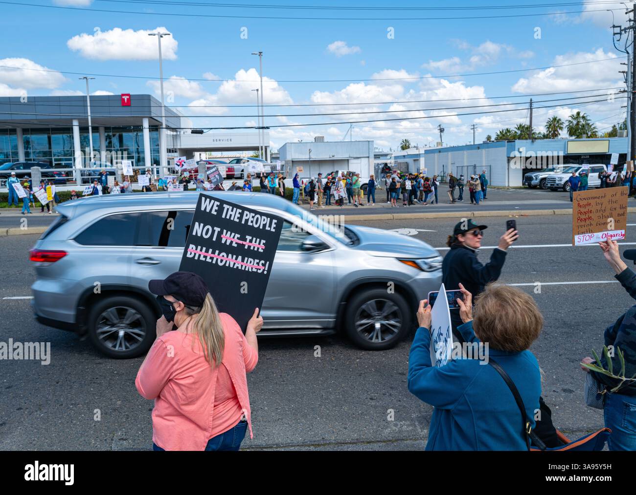 Un activiste tient une pancarte We the People Not milliardaires lors d'une manifestation anti-Elon Musk devant le concessionnaire Tesla sur Arden.Way. Banque D'Images
