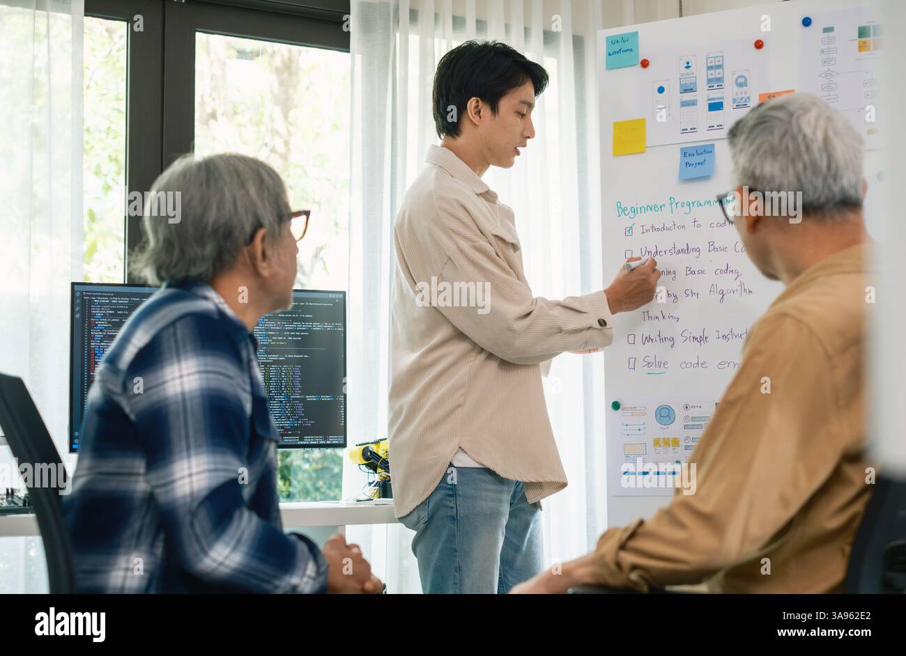 Programmeur senior bootcamlp, jeune instructeur asiatique guide les apprenants seniors à travers une programmation sur tableau blanc, mettant en évidence la pensée algorithmique et sim Banque D'Images