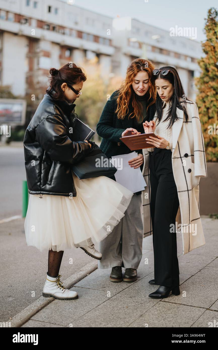 Trois femmes élégantes collaborant tout en examinant une tablette à l'extérieur par une journée ensoleillée Banque D'Images