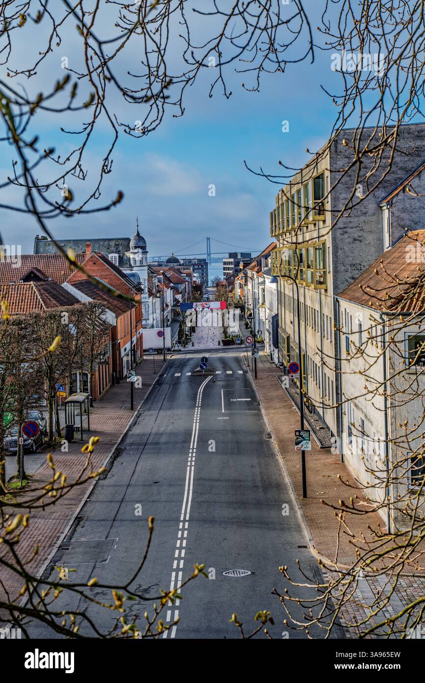 Une scène urbaine magnifiquement encadrée mettant en valeur une rue calme bordée de bâtiments historiques, menant à un pont sous un ciel lumineux. Capturé pendant Banque D'Images