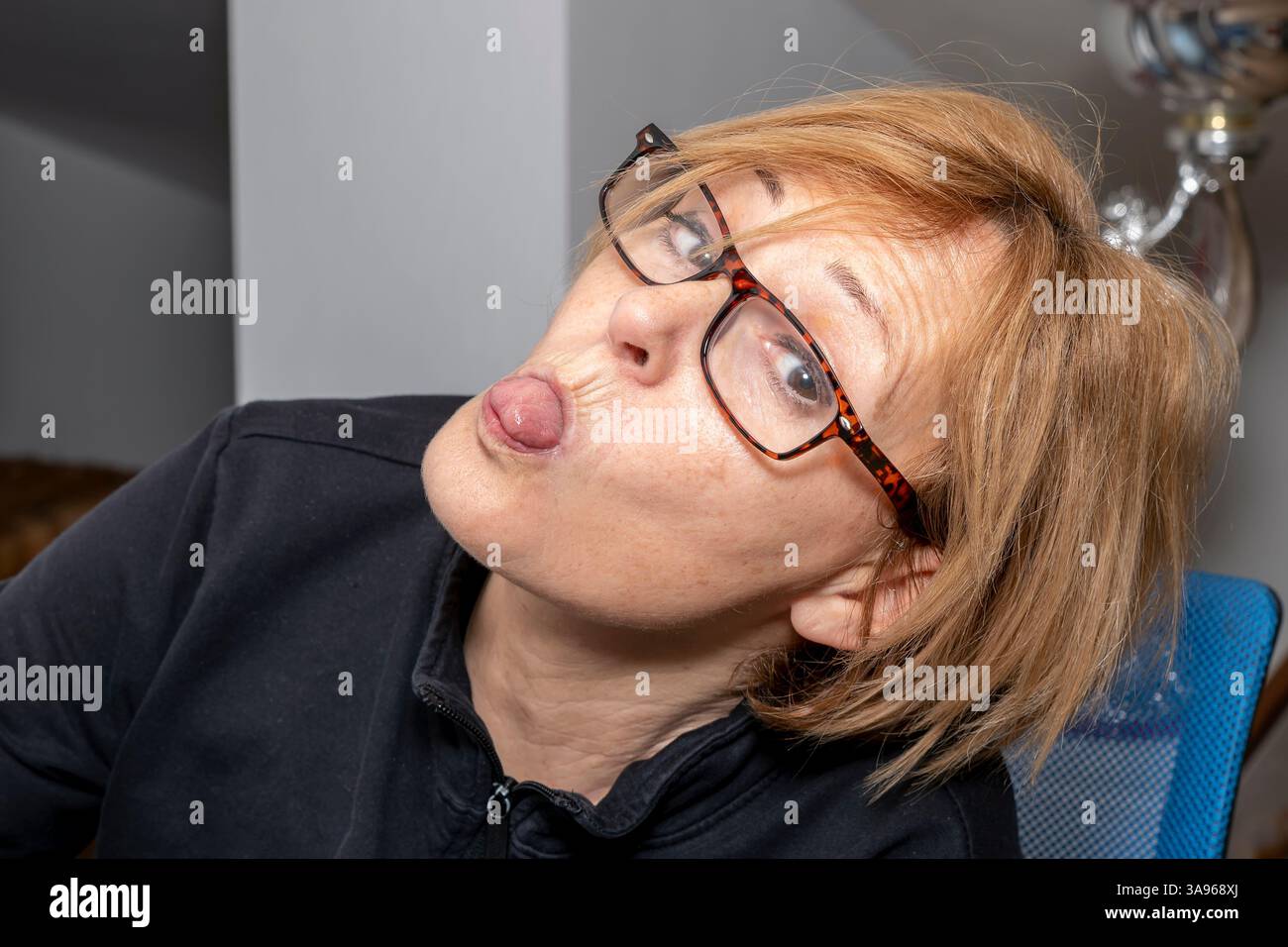 Une femme blonde avec des lunettes sort sa langue avec sa tête inclinée d'un côté Banque D'Images