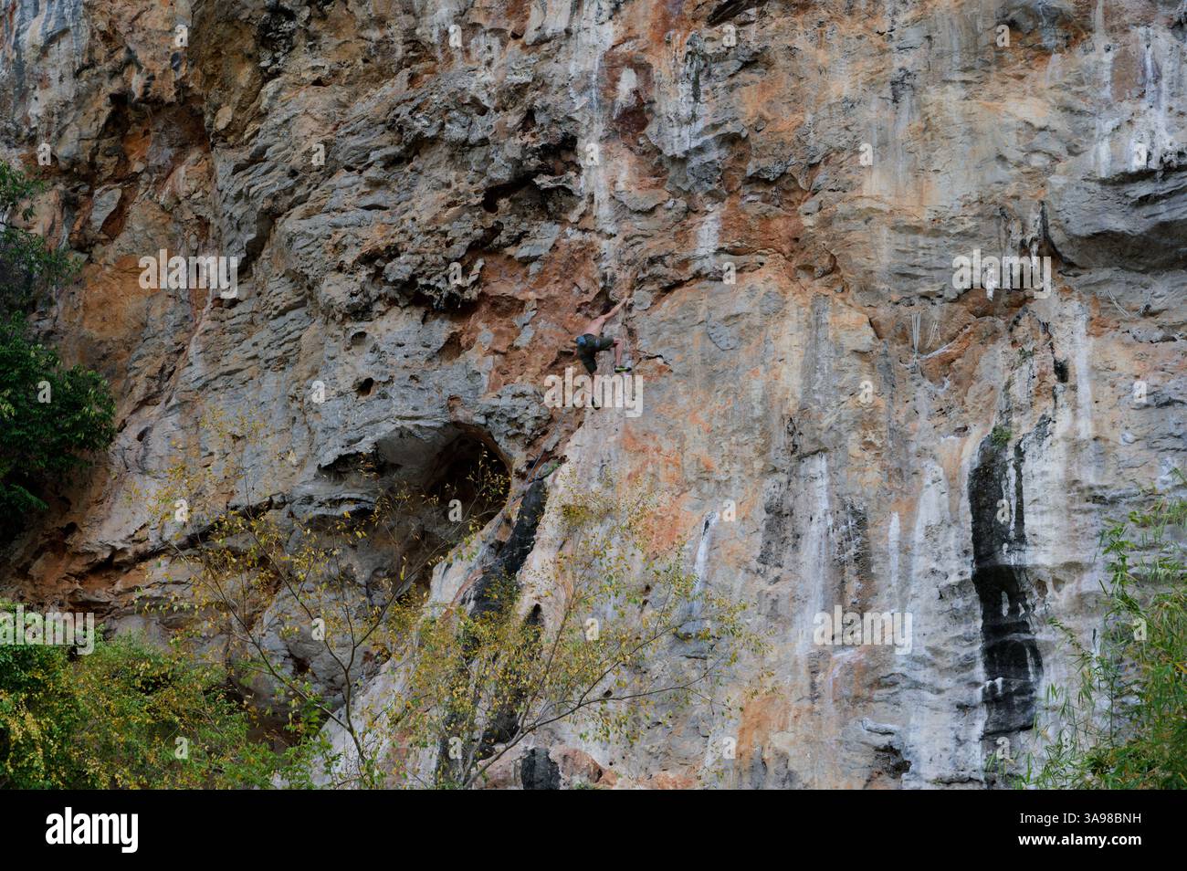 Grimpeur monte une falaise de calcaire texturée avec un mouvement audacieux Banque D'Images
