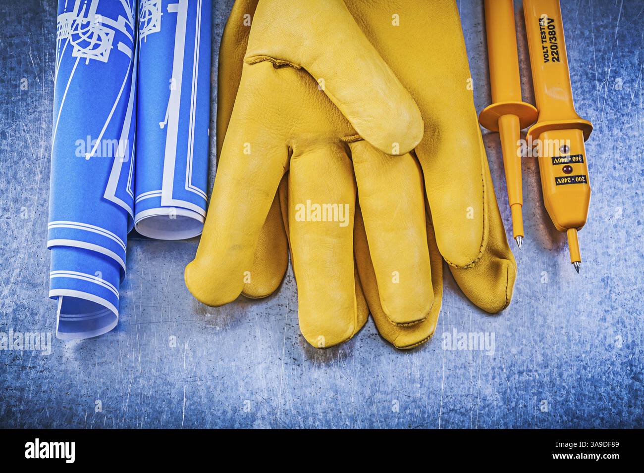Gants de protection jaunes pour testeur électrique plans de construction roulés bleus sur fond métallique Banque D'Images