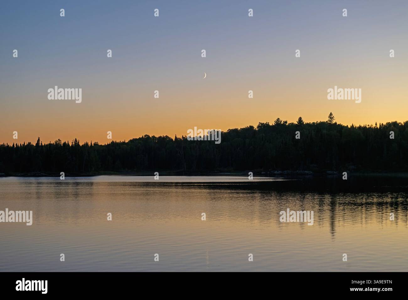 Croissant de lune au-dessus d'un lac calme au coucher du soleil sur le lac Saganaga dans les eaux limitrophes du Minnesota Banque D'Images