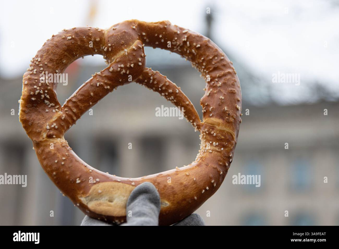 Main tenant appétissant bretzel bavarois traditionnel avec les cristaux de sel. Le bâtiment du Reichstag de Berlin peut être vu à travers le bretzel sur le flou Banque D'Images