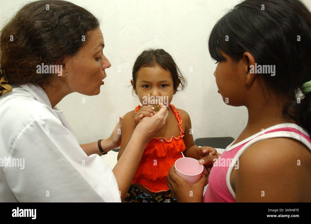 10 mars 2006 ; Asuncion, PARAGUAY ; le Dr CHANTAL HULIN (à gauche) administre un médicament oral à une fillette de 4 ans ayant de graves problèmes de survie à l'Asociacion Cultural Justicia y Verdad (Association de justice culturelle et de vérité) à Asuncion, Paraguay le 10 mars 2006 à Asuncion, Paraguay. Le refuge fondé par le Dr Hulin est géré par un garage automobile rénové, où des bénévoles fournissent des repas simples, des douches, administrent des soins de santé et des activités en classe à certains des centaines d’enfants des rues sans abri qui gèrent et nettoient les pare-brise pour de l’argent dans les rues du quartier. Mandato Banque D'Images