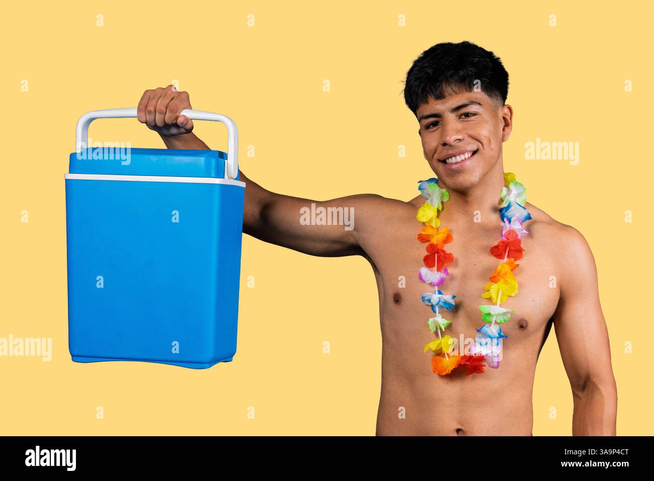 Jeune homme souriant portant un lei hawaïen tenant une glacière portable bleue, prêt pour les vacances d'été ou une fête de plage Banque D'Images