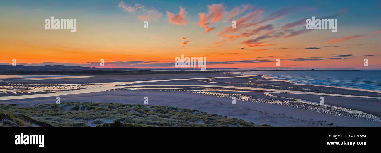Une vue panoramique de Budle Bay au coucher du soleil à marée basse en été de Bamburgh regardant vers le nord en direction de l'île Sainte de Lindisfarne Banque D'Images