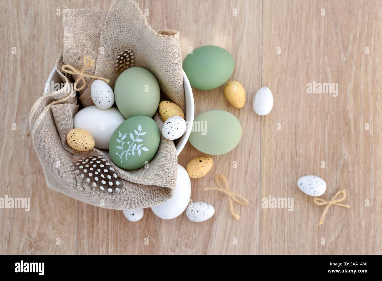 Oeufs de pâques élégants décorés dans un bol blanc sur toile de lin sur une table en bois clair. Vue de dessus. Avec de l'espace pour votre texte Banque D'Images