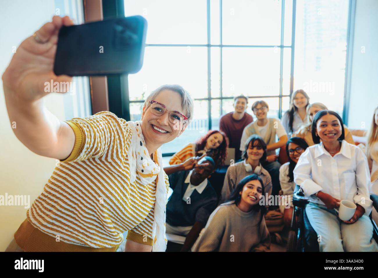Un groupe dynamique d'étudiants pose joyeusement avec leur mentor, prenant un selfie joyeux dans un cadre de classe lumineux. Banque D'Images