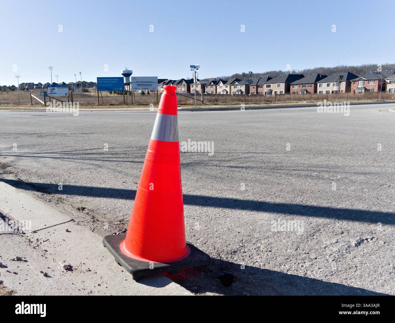 Un cône de sécurité orange isolé positionné au bord d'une banlieue en développement souligne le délicat équilibre entre progrès et précaution Banque D'Images