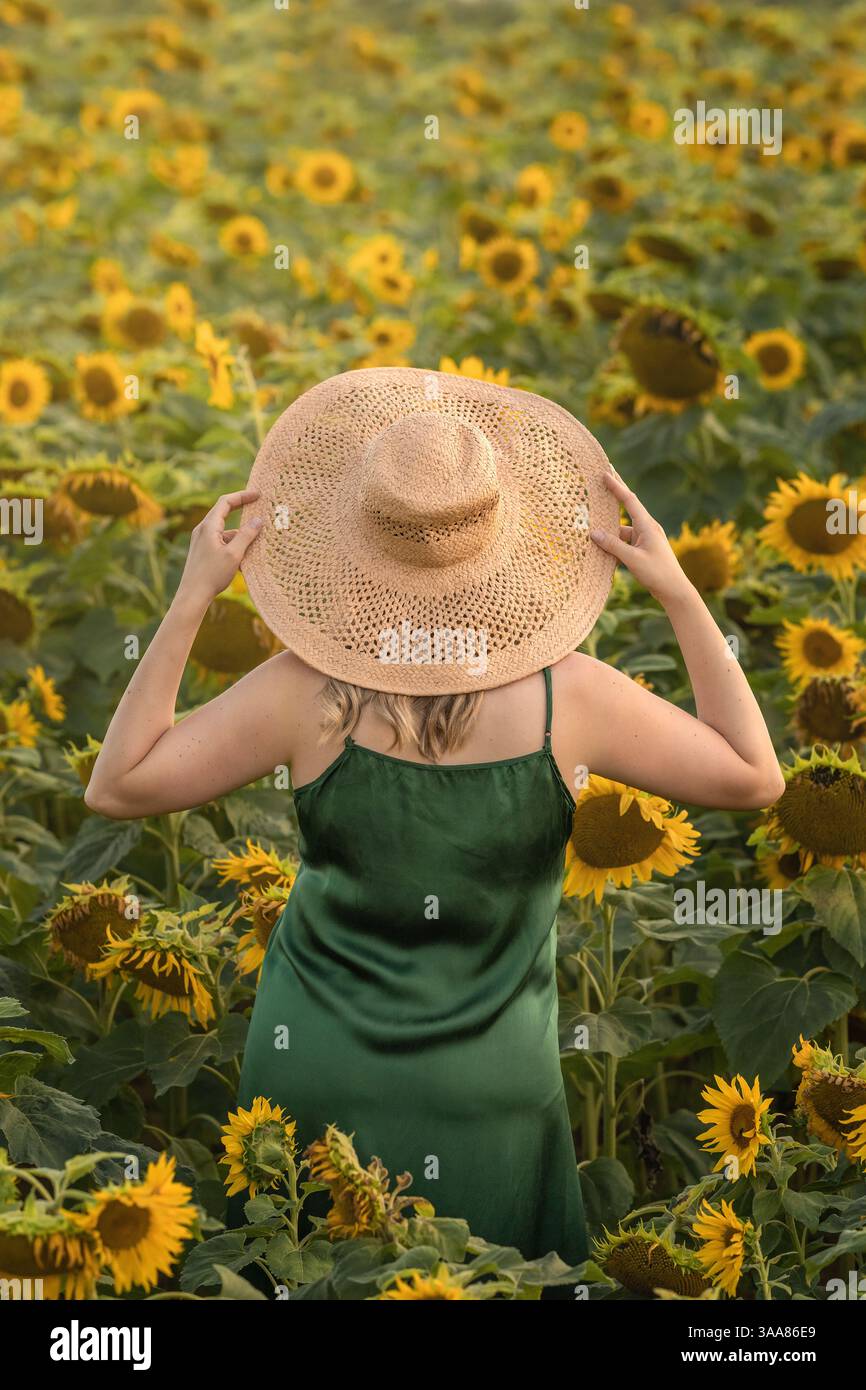 Femme en robe verte debout dans le champ de tournesol, tenant le chapeau jaune dans les mains. Photographie artistique Banque D'Images