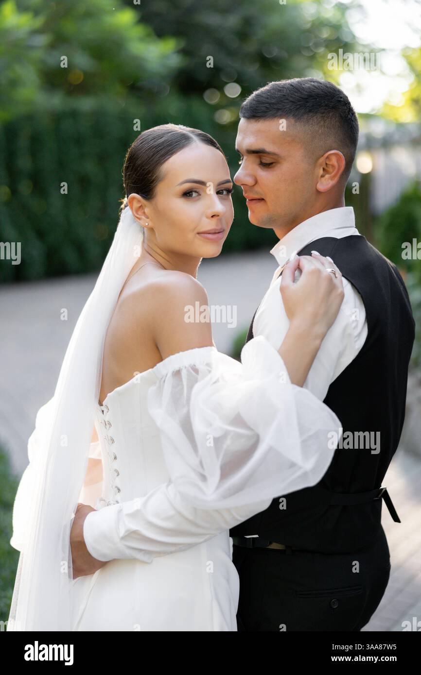 Couple de jeunes mariés se tenant la main et s'embrassant dans un parc, célébrant leur amour et leur engagement lors de leur cérémonie de mariage Banque D'Images