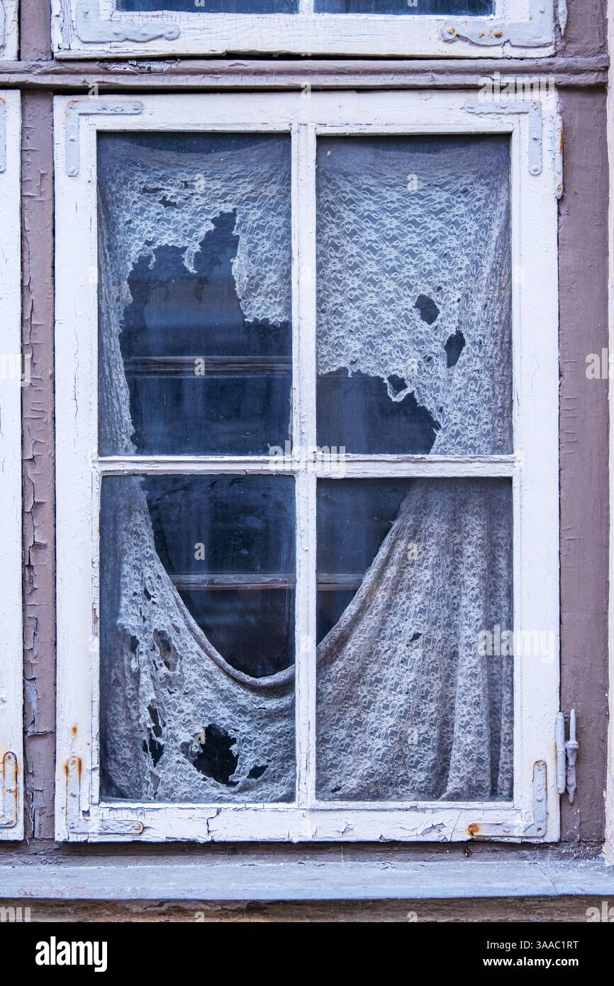 Vieux rideaux sales déchirés avec des trous et une fenêtre cassée. Signes de négligence à domicile. Des endroits perdus ont délabré sharm. Maison en ruine endommagée. Banque D'Images