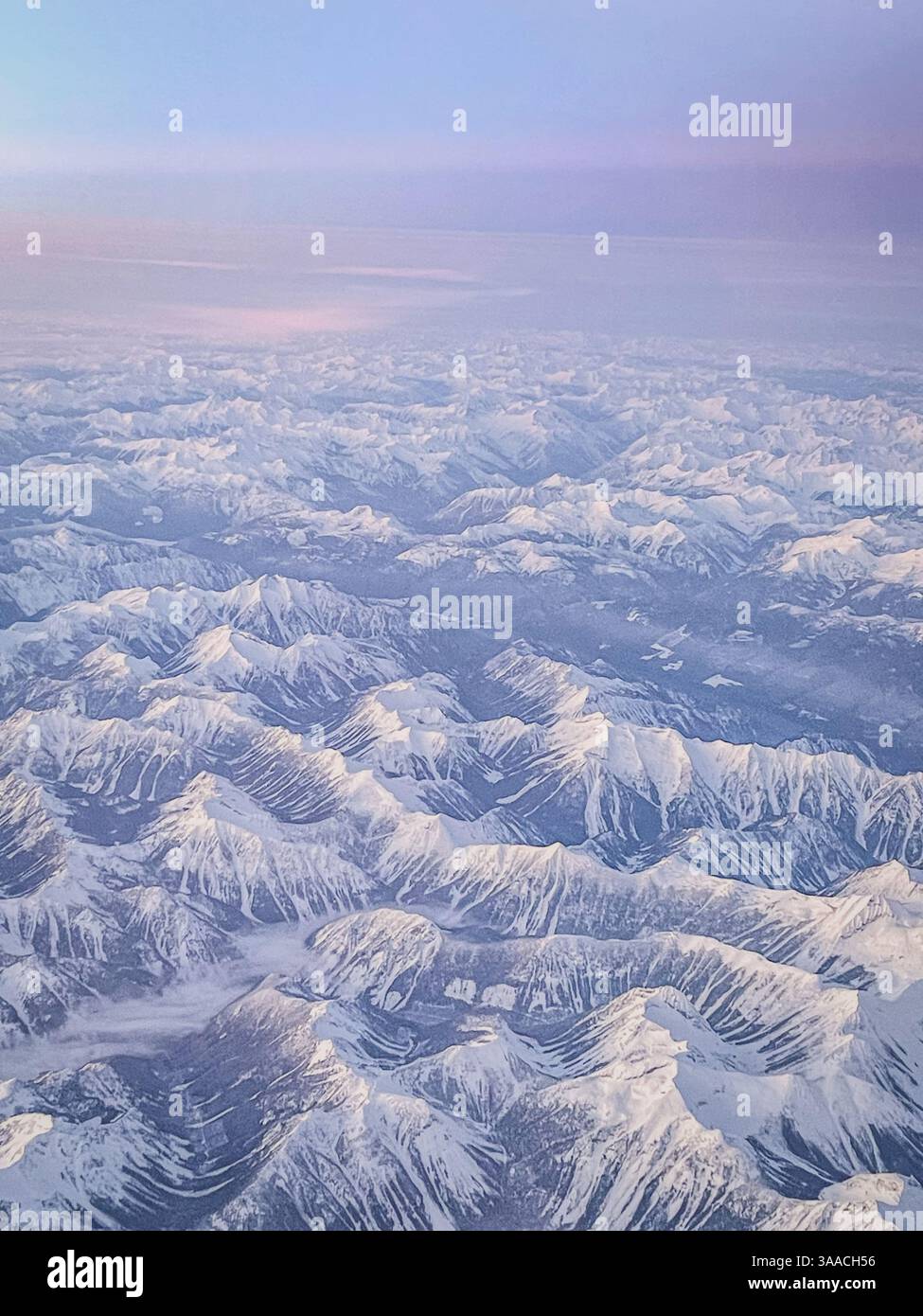 Vue aérienne de la chaîne de montagnes enneigée au crépuscule, avec des teintes pastel douces dans le ciel. Idéal pour les voyages, la nature et les thèmes de paysage hivernal. - Image de stock capturée avec un smartphone