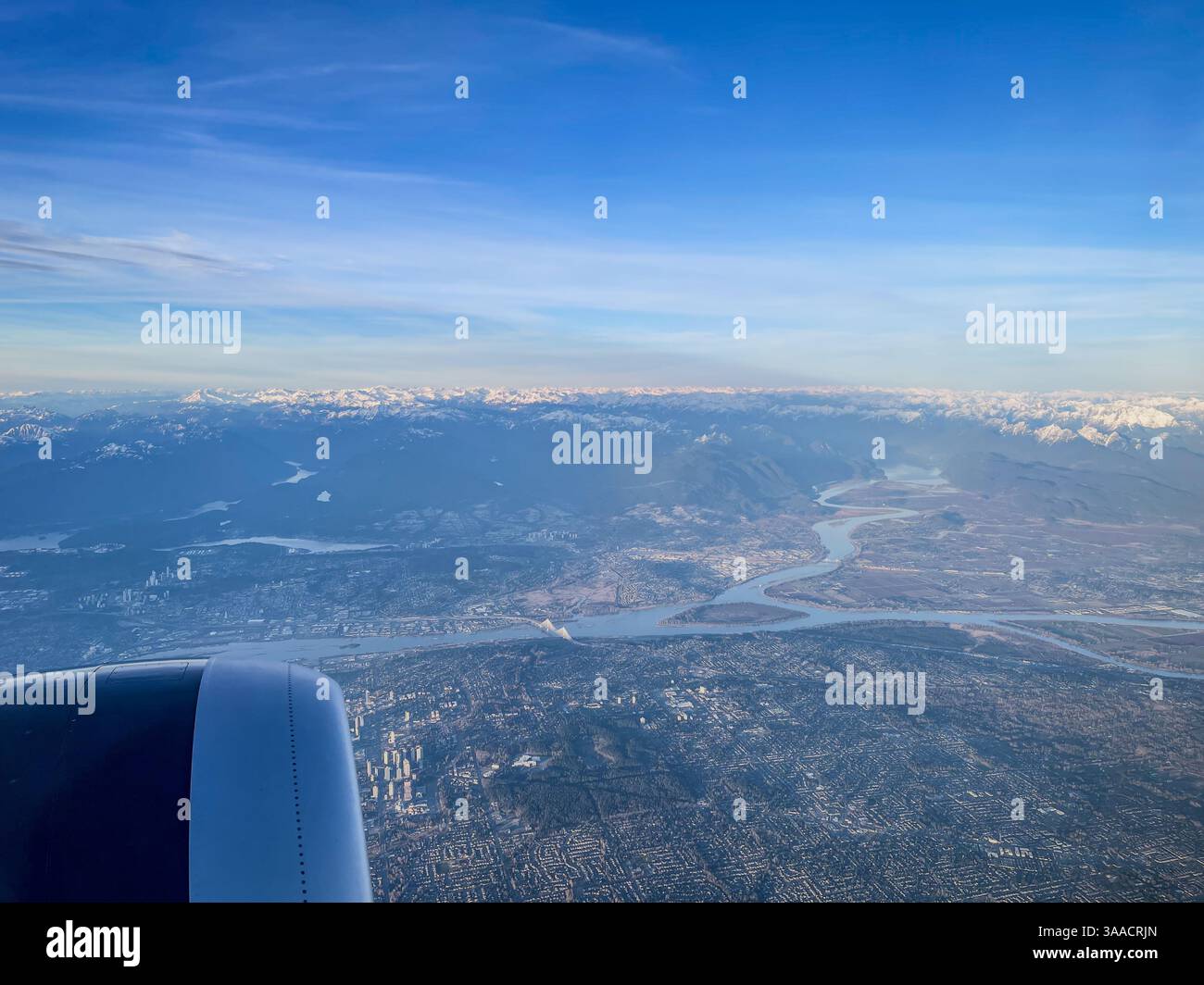 Paysage urbain et rivière sinueuse vus de la fenêtre de l'avion avec chaînes de montagnes et disposition urbaine s'étendant en dessous. - Image de stock capturée avec un smartphone