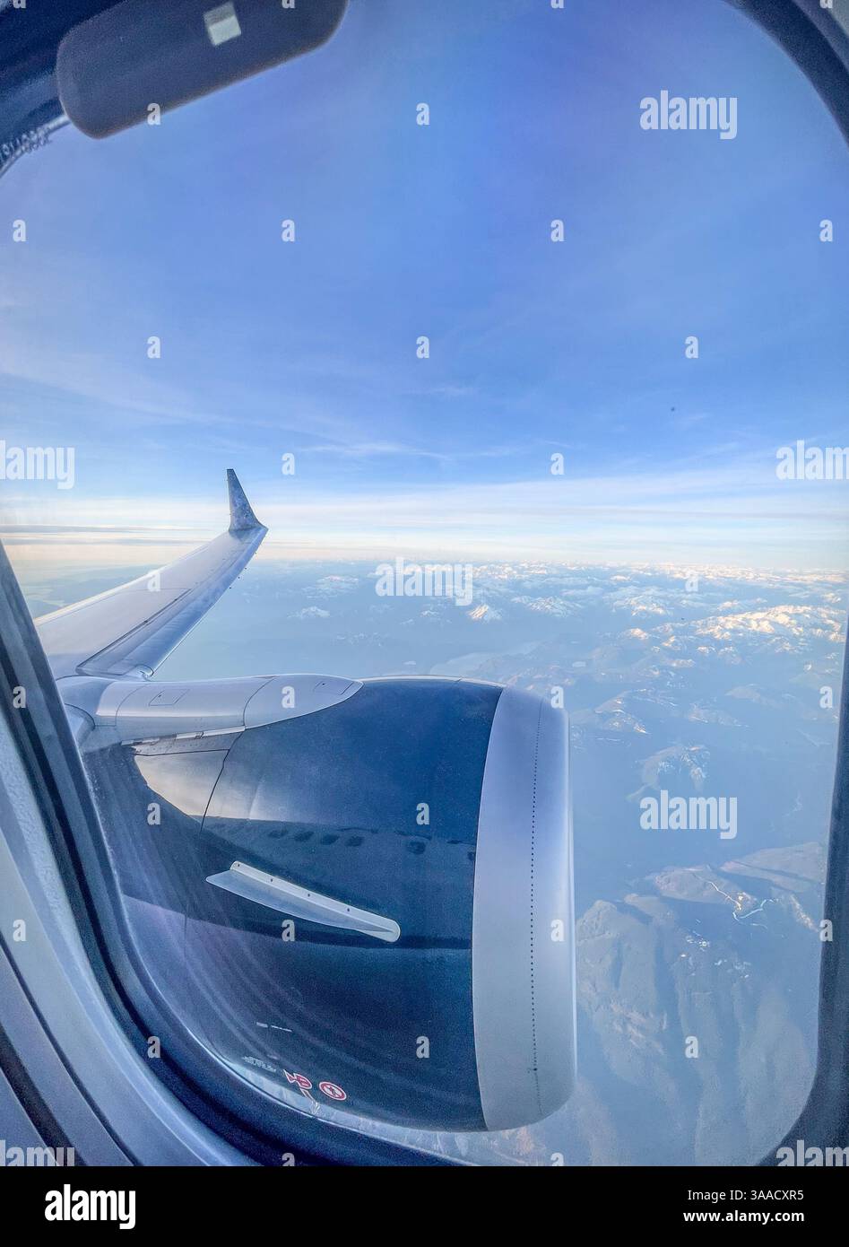 Gros plan d'un moteur d'avion et d'une aile vus à travers la fenêtre avec une vue des sommets de montagne enneigés et du ciel bleu en arrière-plan. - Image de stock capturée avec un smartphone