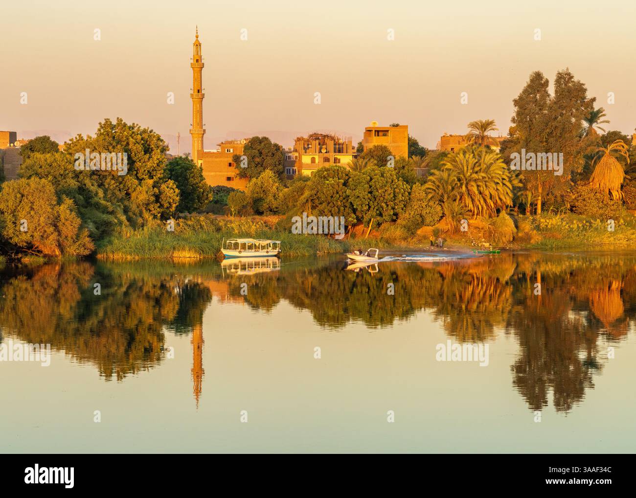 Tranquille ville riveraine de Naqadah en Egypte, avec des bâtiments traditionnels et une végétation luxuriante, avec bateau de police sur la rivière Banque D'Images