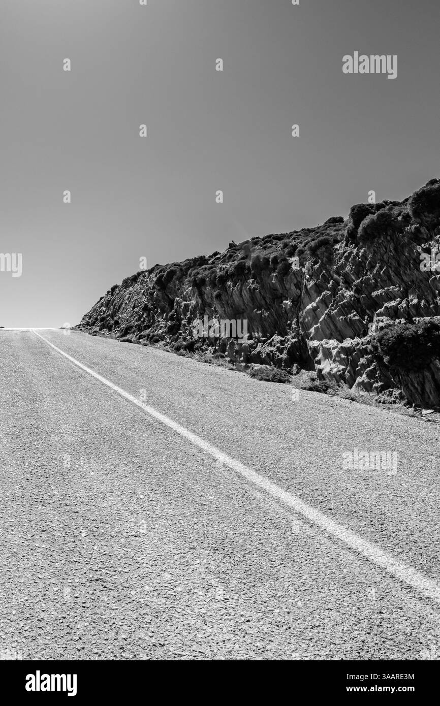Vue d'une route vide et solitaire à côté de collines rocheuses dans iOS Grèce en noir et blanc Banque D'Images