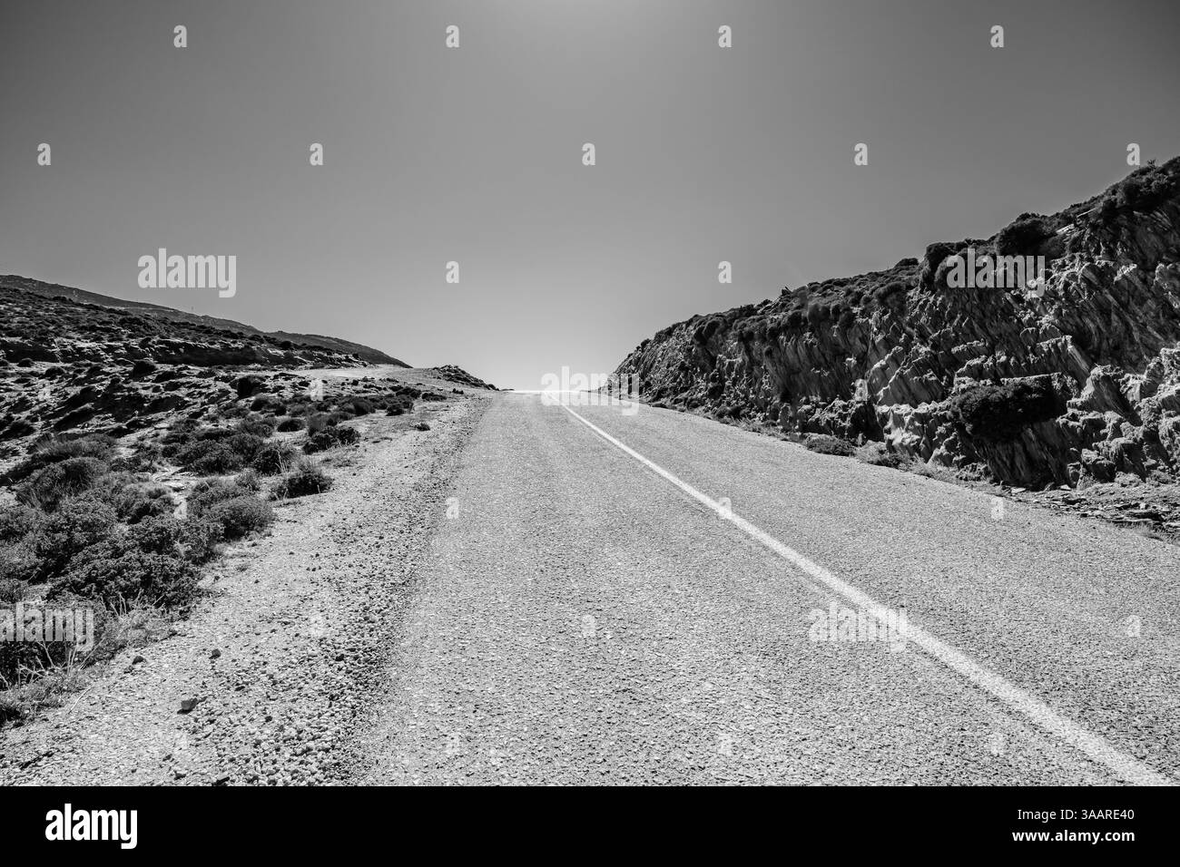 Vue d'une route vide et solitaire à côté de collines rocheuses dans iOS Grèce en noir et blanc Banque D'Images