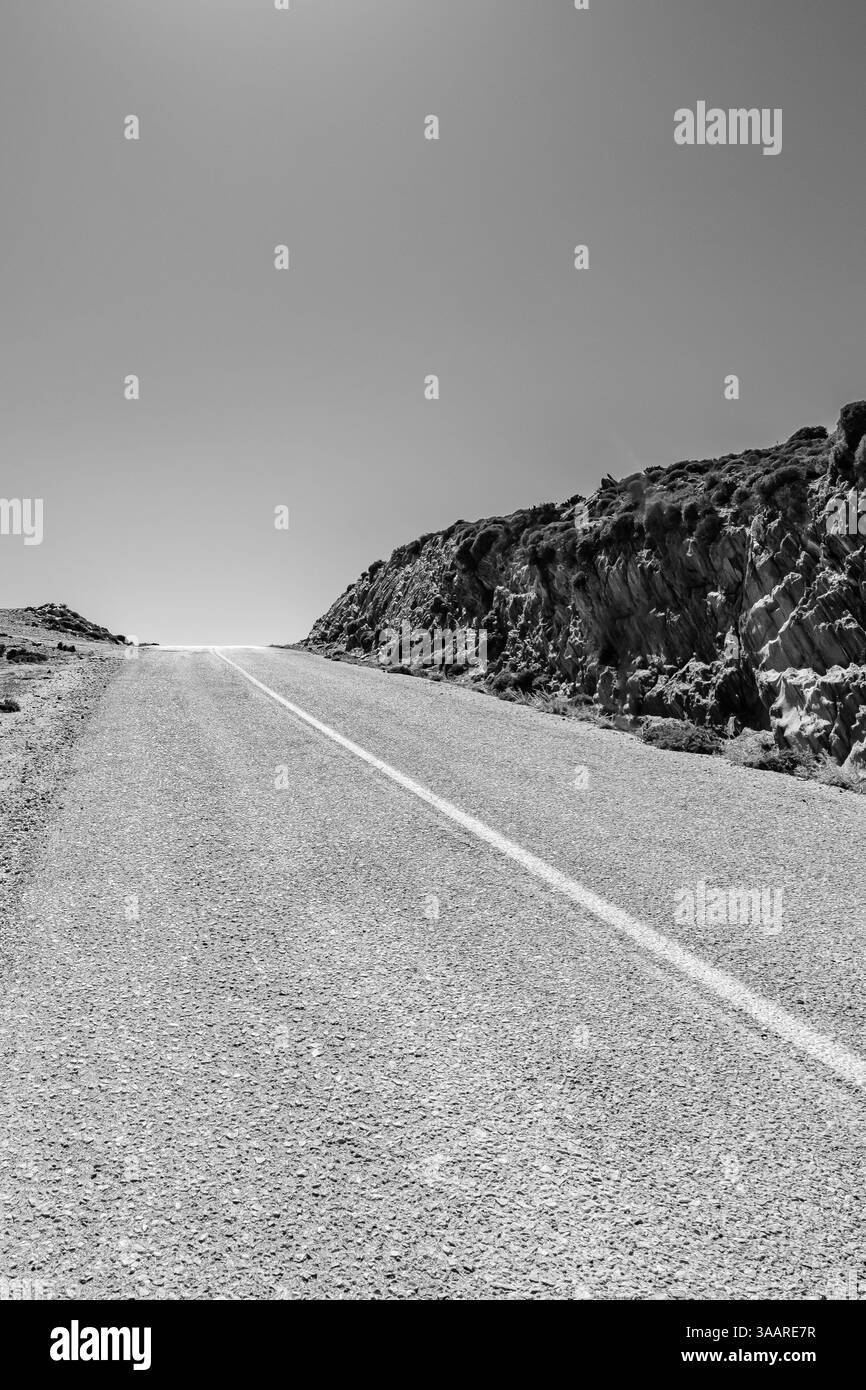 Vue d'une route vide et solitaire à côté de collines rocheuses dans iOS Grèce en noir et blanc Banque D'Images