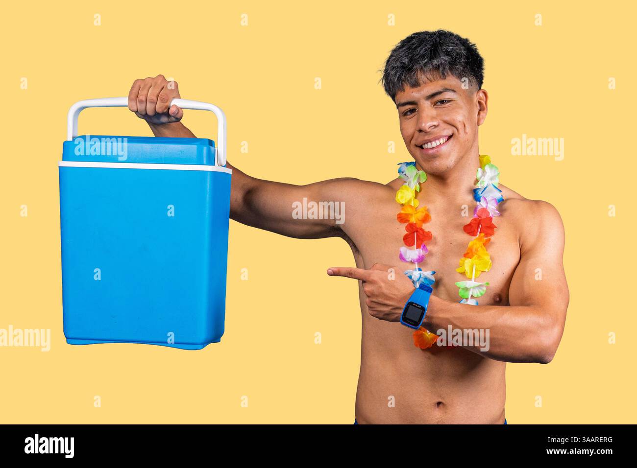 Jeune homme portant un collier hawaïen pointant vers la glacière portable, suggérant des boissons rafraîchissantes pour les vacances d'été Banque D'Images
