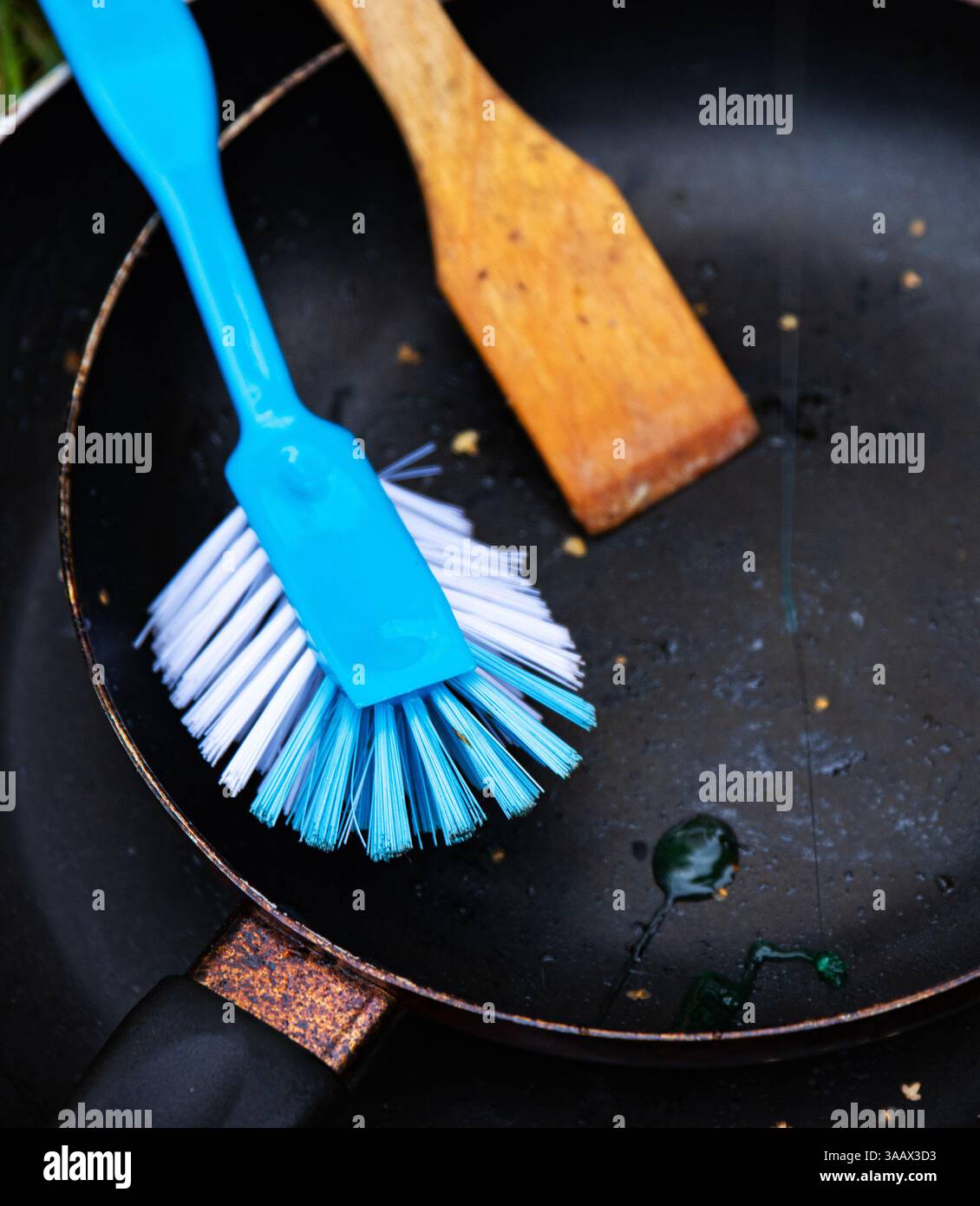 Gros plan d'une poêle sale avec des gouttes de savon liquide, un récureur en bois et une brosse bleue, symbolisant le style de vie du camping, le nettoyage extérieur et la corvée Banque D'Images