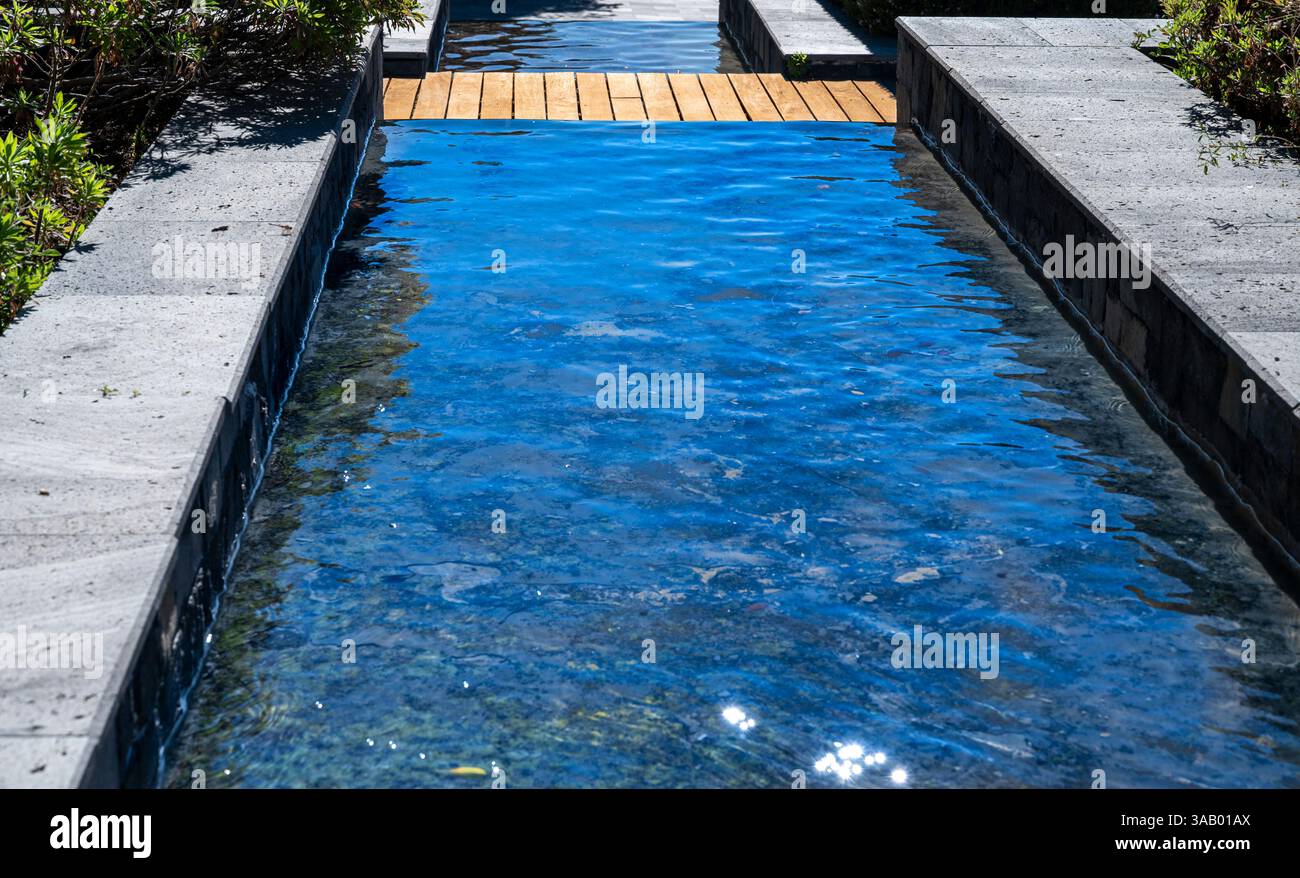Un petit jet d'eau coule le long d'un mur de pierre. L'eau est claire et calme, reflétant la lumière du soleil Banque D'Images