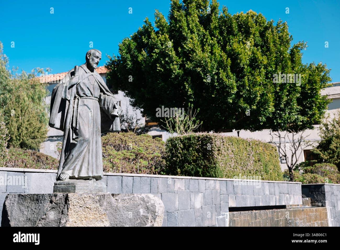 Devant un arbre, il y a une statue d'un homme avec un livre à la main, frère Pedro. La statue est en pierre et est située dans un parc. Banque D'Images