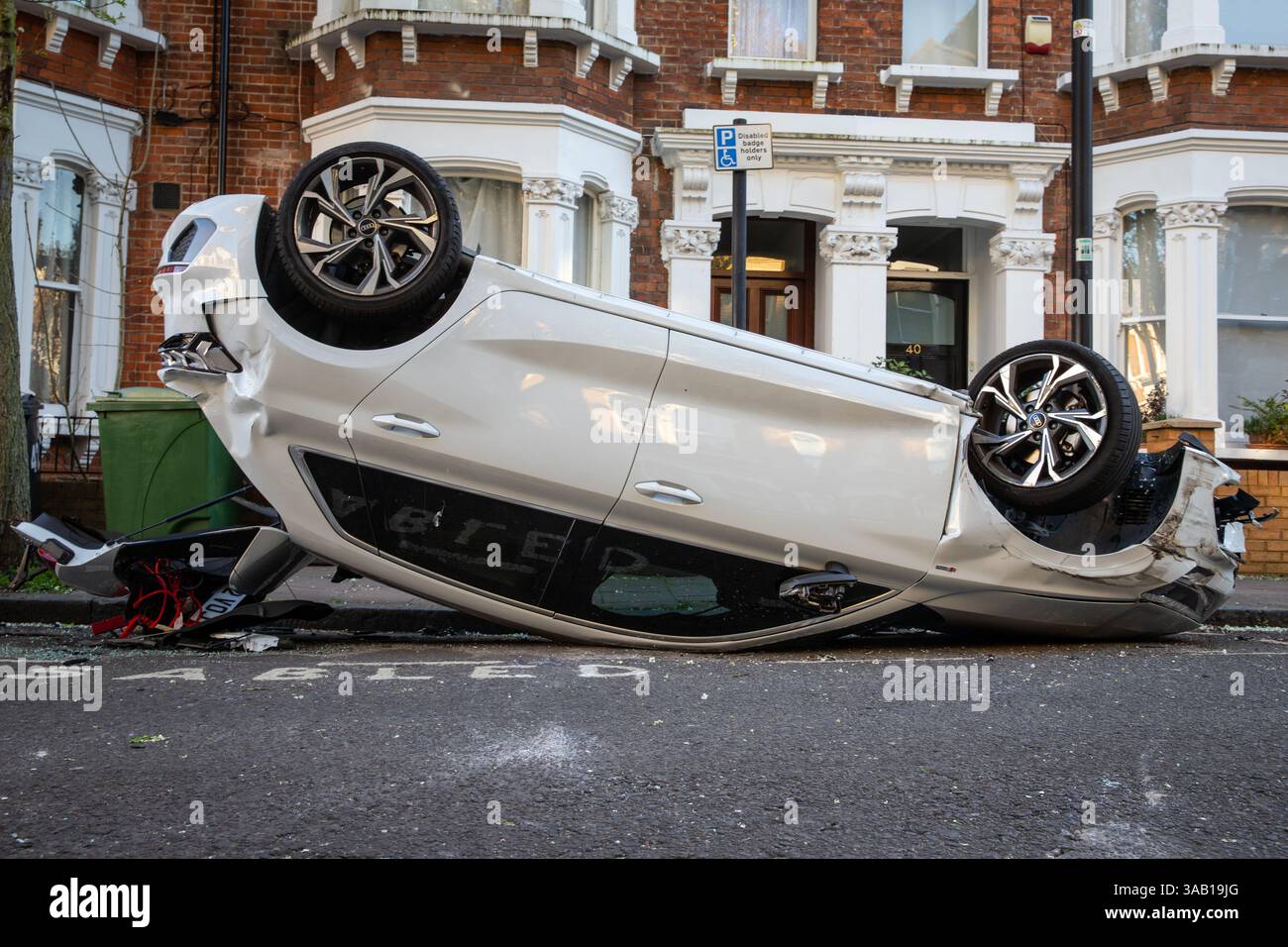 Voiture blanche renversée 'garée' dans une baie pour handicapés dans une rue résidentielle de Londres après un accident de la route Banque D'Images