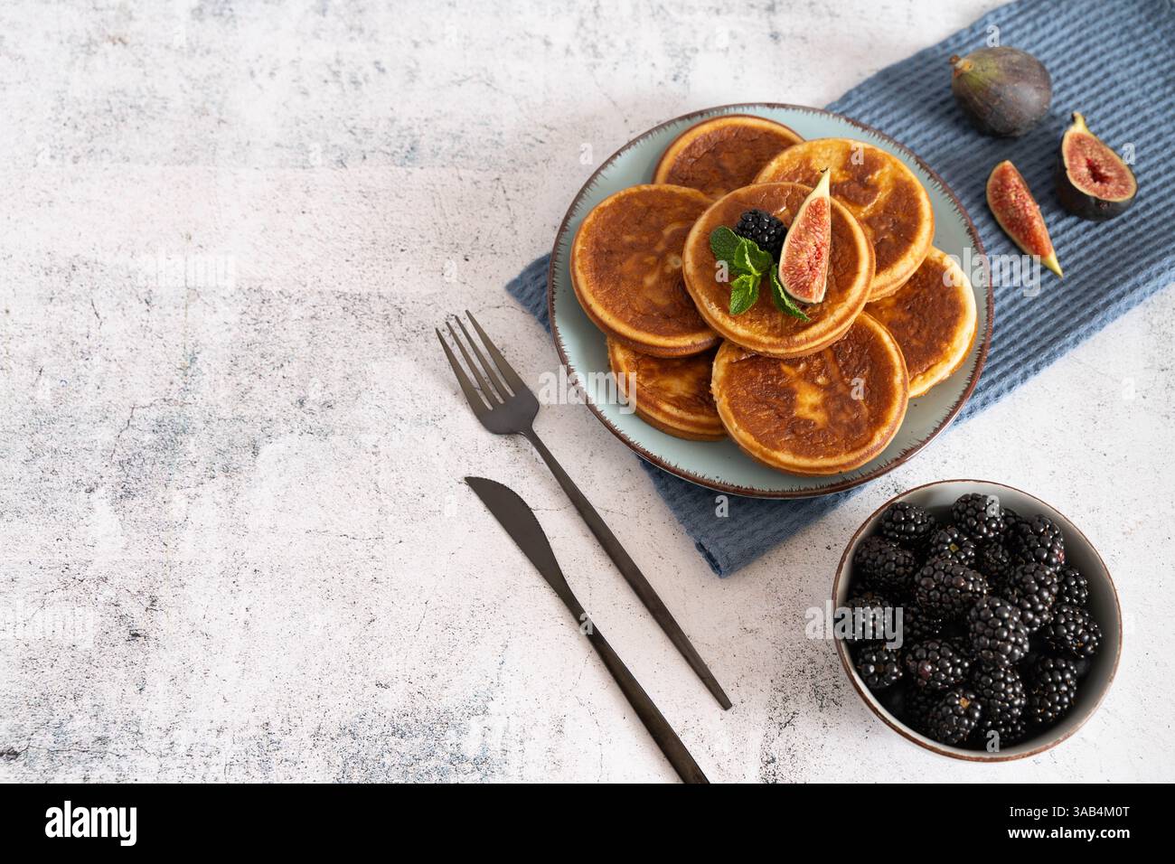 Pile de crêpes maison avec des bleuets, des framboises et des fraises sur une assiette blanche avec un chiffon bleu sur un dessus de table gris clair Banque D'Images Pile de crêpes maison avec des bleuets, des framboises et des fraises sur une assiette blanche avec un chiffon bleu sur un dessus de table gris clair Banque D'Images