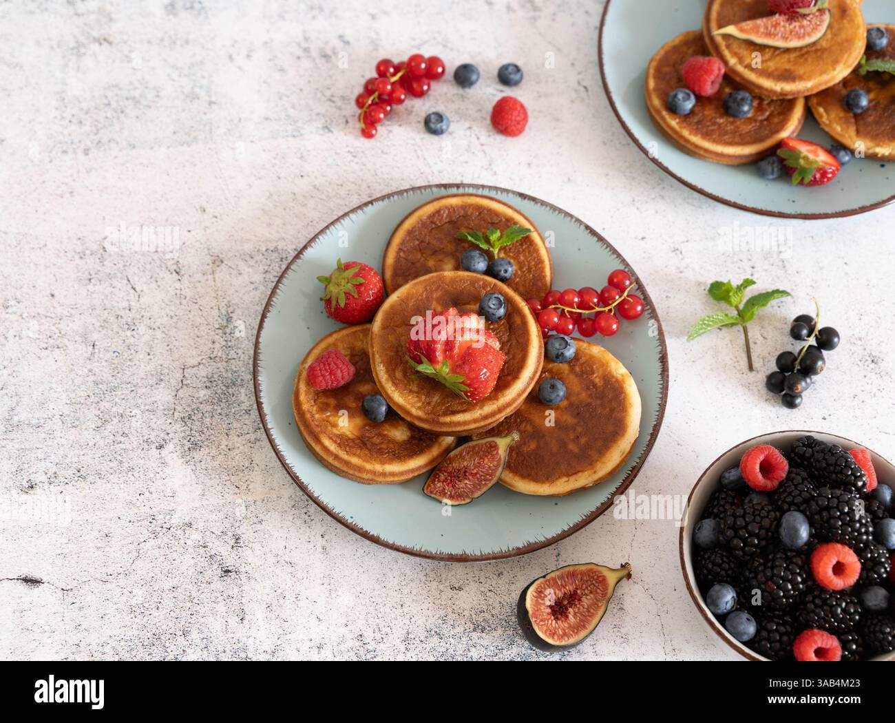 Pile de crêpes maison avec des bleuets, des framboises et des fraises sur une assiette blanche avec un chiffon bleu sur un dessus de table gris clair Banque D'Images Pile de crêpes maison avec des bleuets, des framboises et des fraises sur une assiette blanche avec un chiffon bleu sur un dessus de table gris clair Banque D'Images
