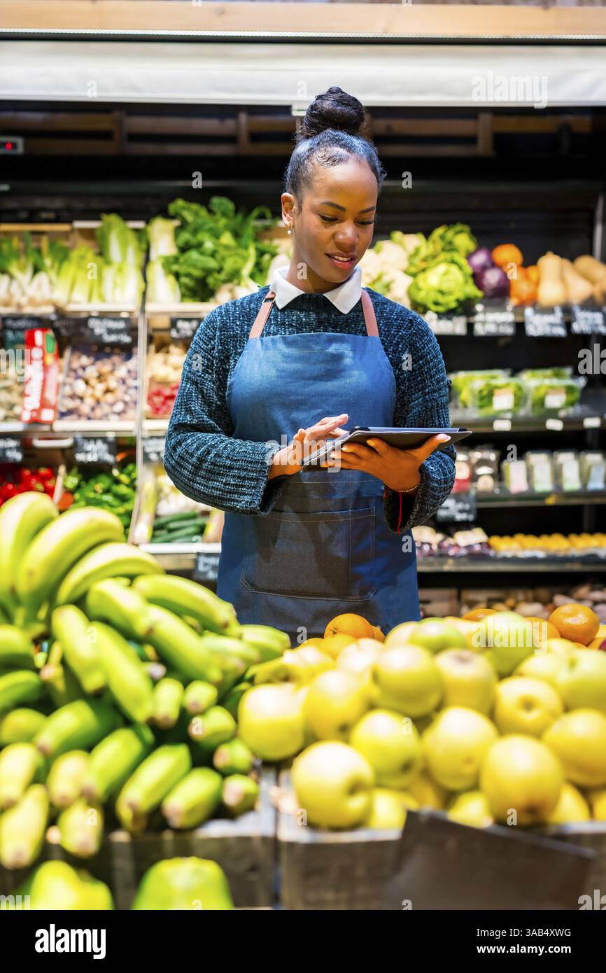 Employé d'épicerie gérant l'inventaire des produits frais avec une tablette numérique, assurant la qualité et la disponibilité pour les clients Banque D'Images