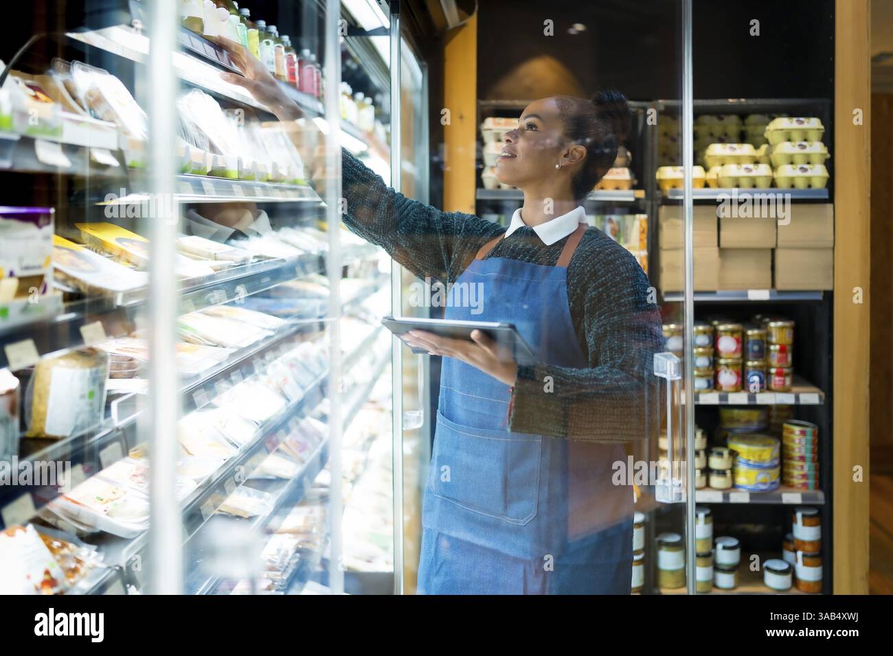 Vendeur souriant portant tablier vérifiant les produits alimentaires à l'aide de tablette numérique tout en travaillant dans un supermarché biologique Banque D'Images