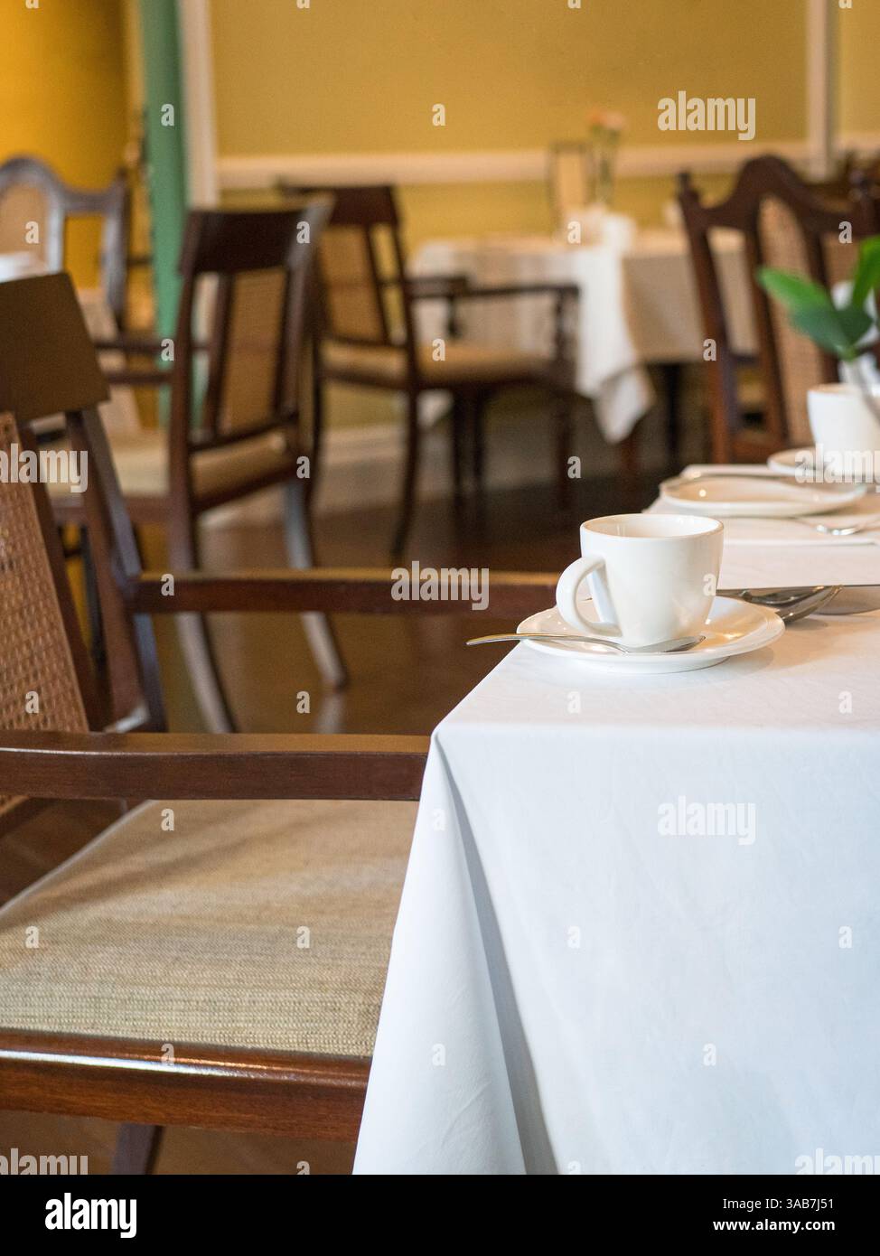 Intérieur d'un restaurant. Gros plan sur la tasse blanche et la soucoupe sur la table recouverte de tissu blanc. Banque D'Images