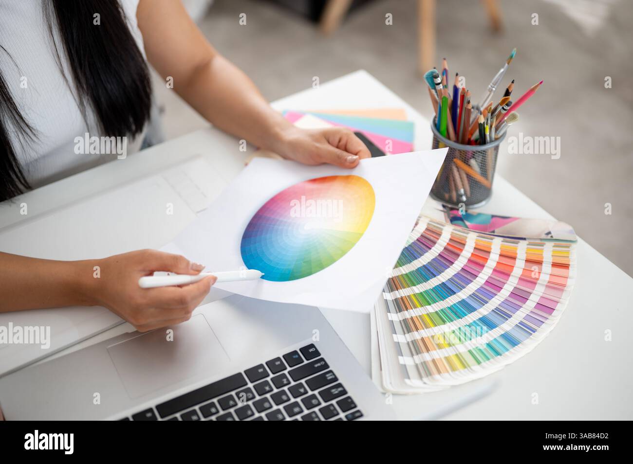 Un gros plan d'une paire de main tenant un diagramme de couleur de cercle imprimé et un stylet pointant vers la couleur bleue sur la table de travail. Architecte d'intérieur ou graphe Banque D'Images