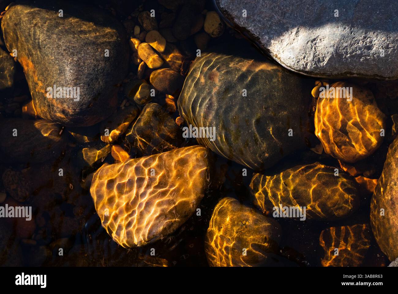 La lumière chaude abstraite et l'eau dessinent des textures sur des pierres en eau peu profonde Banque D'Images