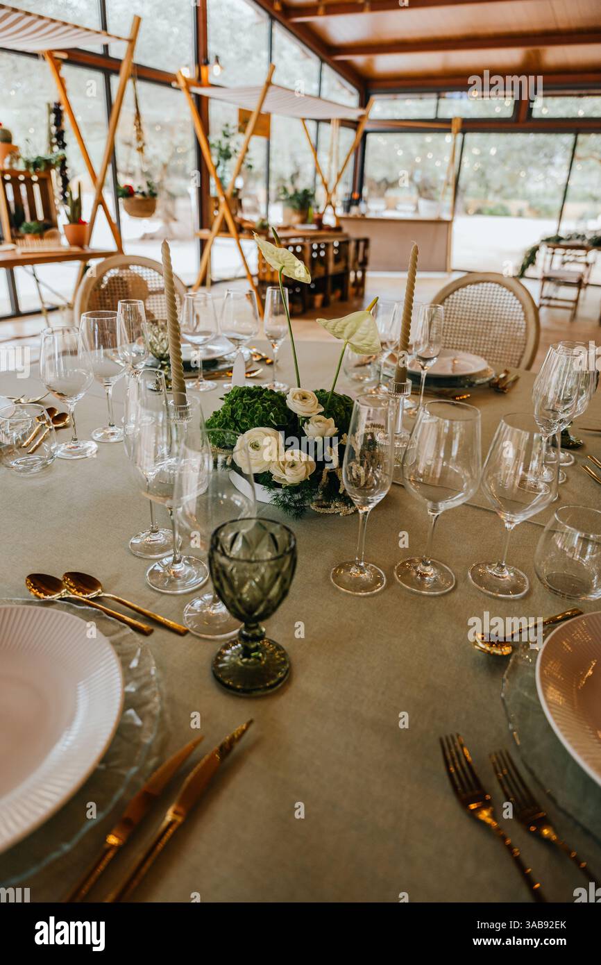 Table ronde magnifiquement décorée avec de la verrerie fine, de la vaisselle blanche, des couverts dorés et un arrangement floral central, préparé pour un événement formel à l'intérieur Banque D'Images