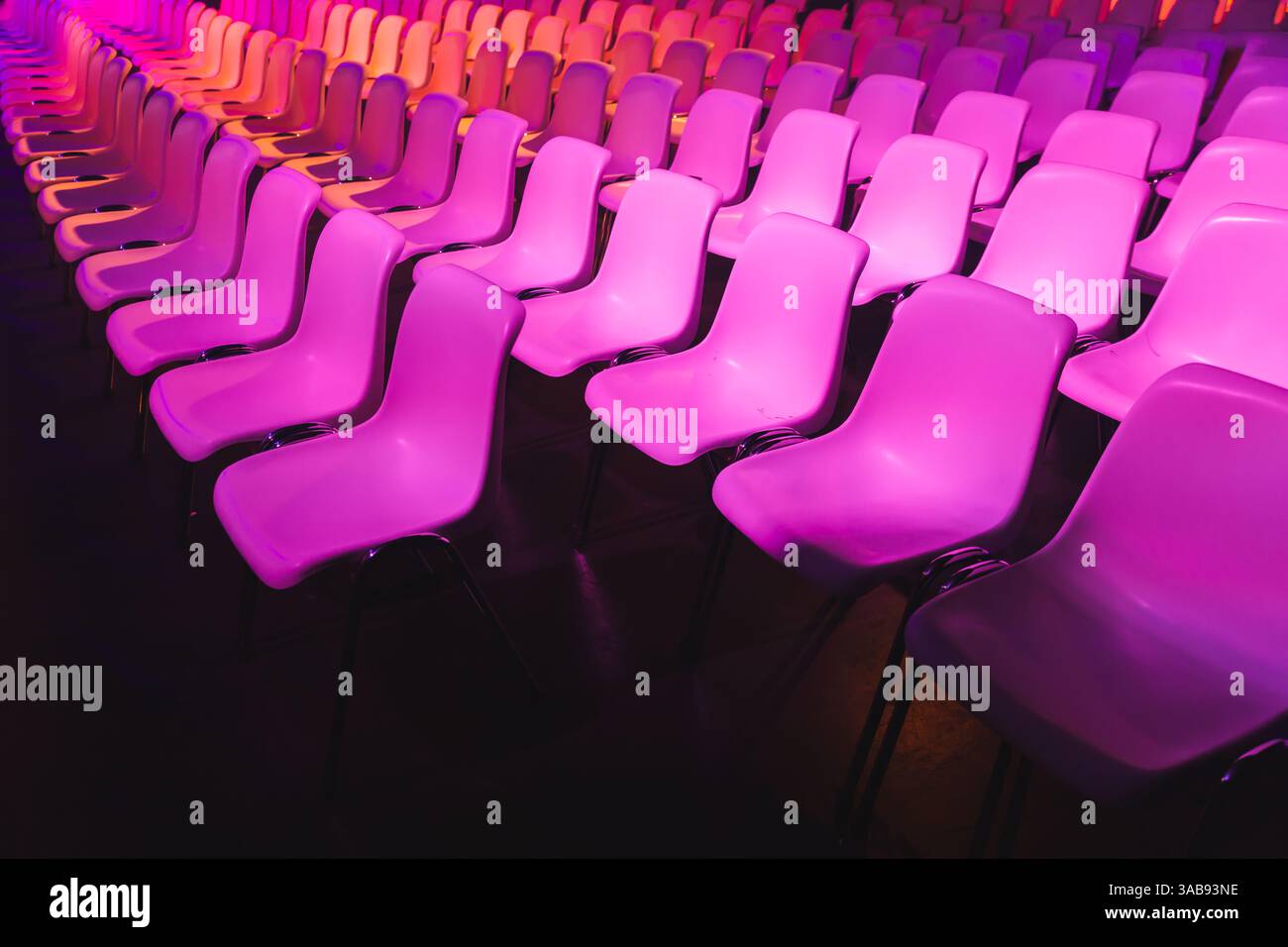 Une gamme captivante de chaises roses dans des rangées soignées, éclairées par un éclairage magenta vif lors d'une conférence de l'IA à Amsterdam. L'arrière-plan sombre améliore le vi Banque D'Images