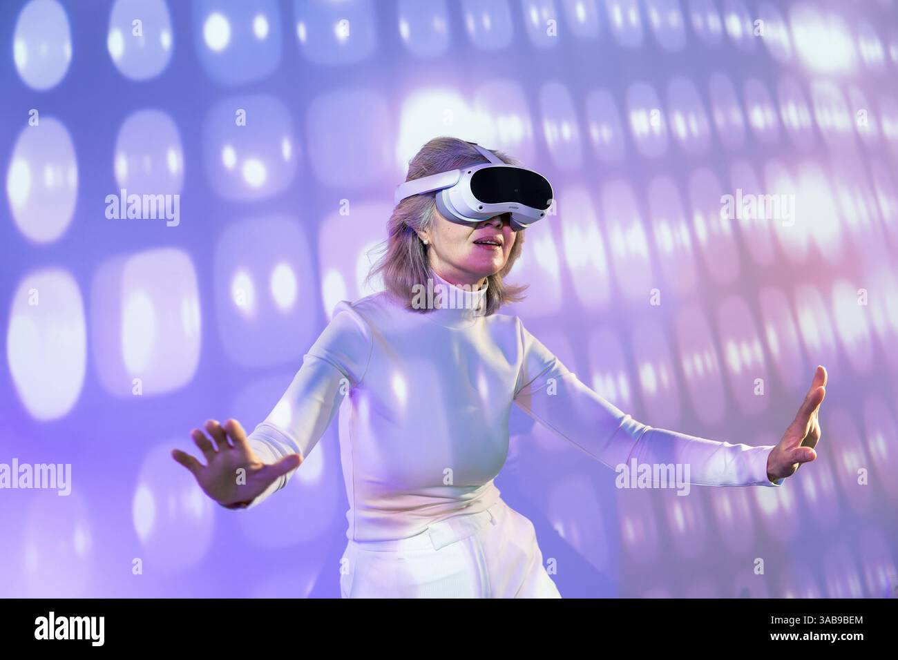 Une femme asiatique âgée fait l’expérience de la métaverse à travers un casque de réalité virtuelle, entouré d’un environnement numérique, mettant en évidence les accès à la technologie Banque D'Images