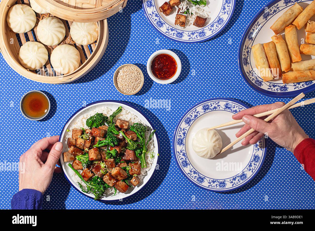 Vue de dessus de la main recadrée méconnaissable arrangeant une nourriture chinoise colorée avec le tofu du général Tso, les petits pains bao et les rouleaux de printemps croustillants. Une main est vue g Banque D'Images