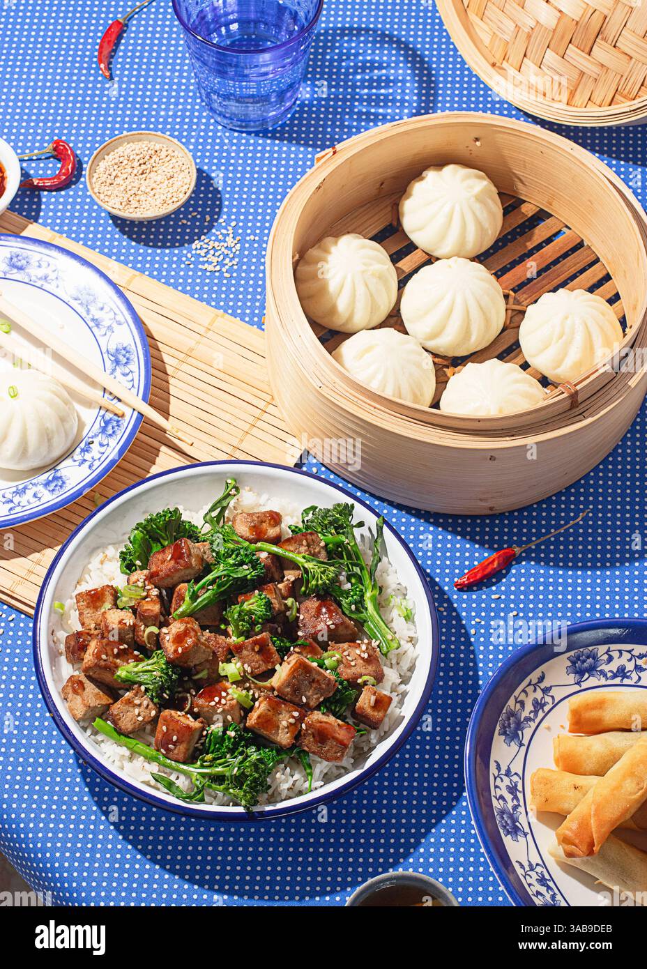 Vue sur le dessus d'un repas chinois traditionnel composé de petits pains cuits à la vapeur, de tofu et de rouleaux de printemps sur une nappe à motifs bleus. L'éclairage lumineux du studio améliore Banque D'Images