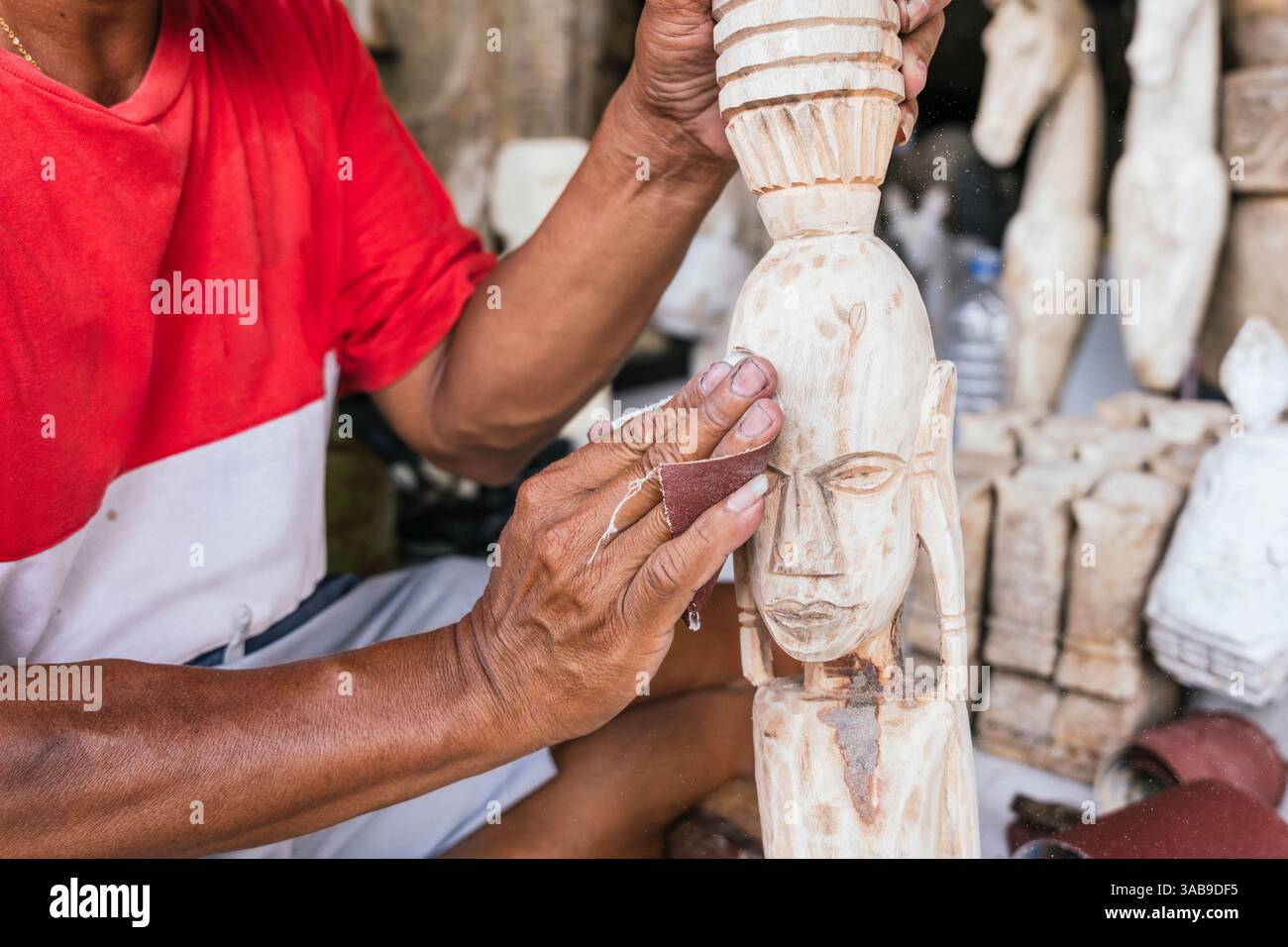 Un artisan indonésien lisse délicatement la surface d'une sculpture en bois à l'aide de papier de verre. Cette scène capture la tradition et artistr méticuleux Banque D'Images