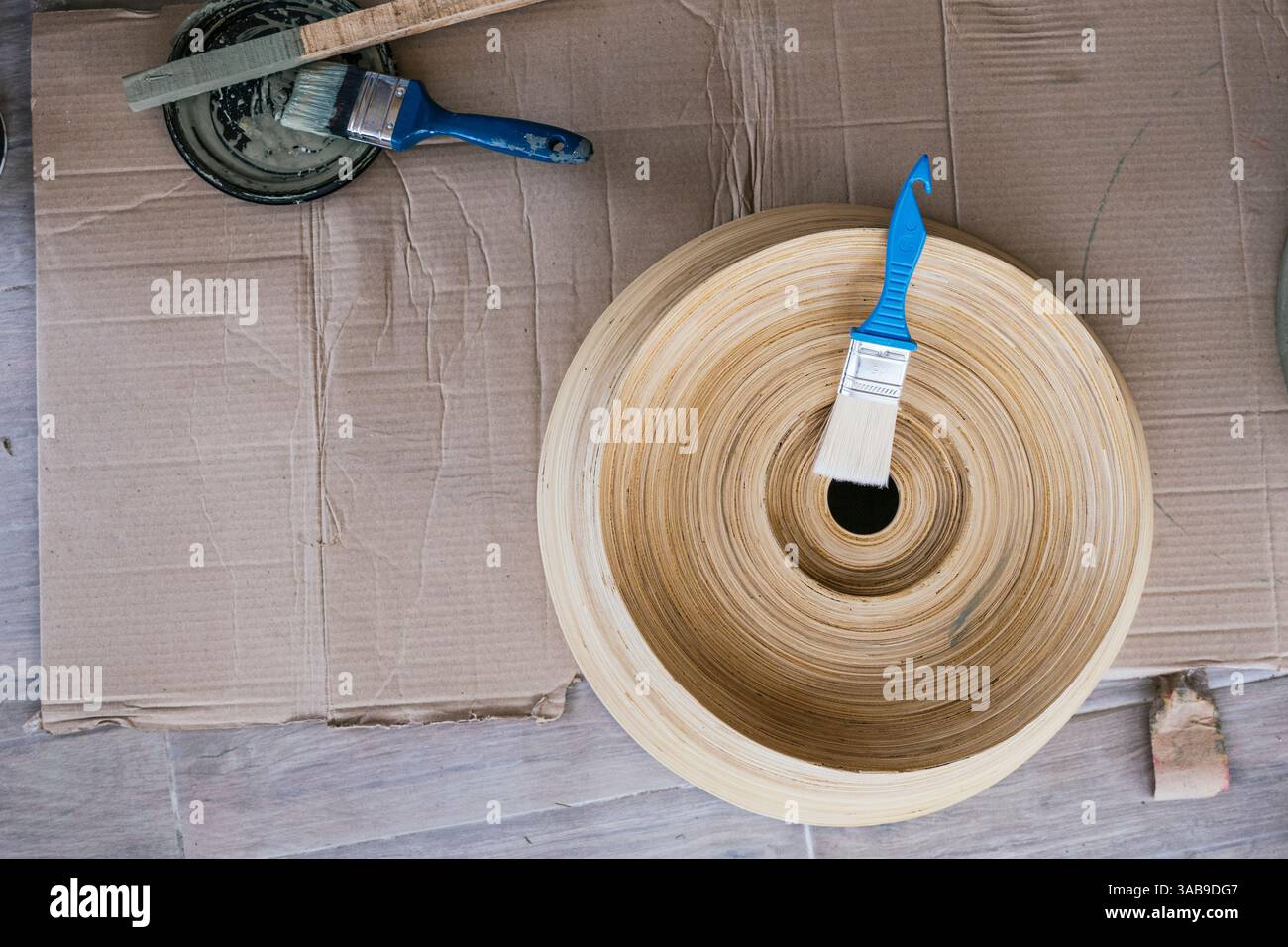Vue aérienne d'outils de peinture artisanale, y compris des pinceaux et de la peinture, à côté d'une sculpture en bois placée sur une surface en carton, capturant un rustique et Banque D'Images