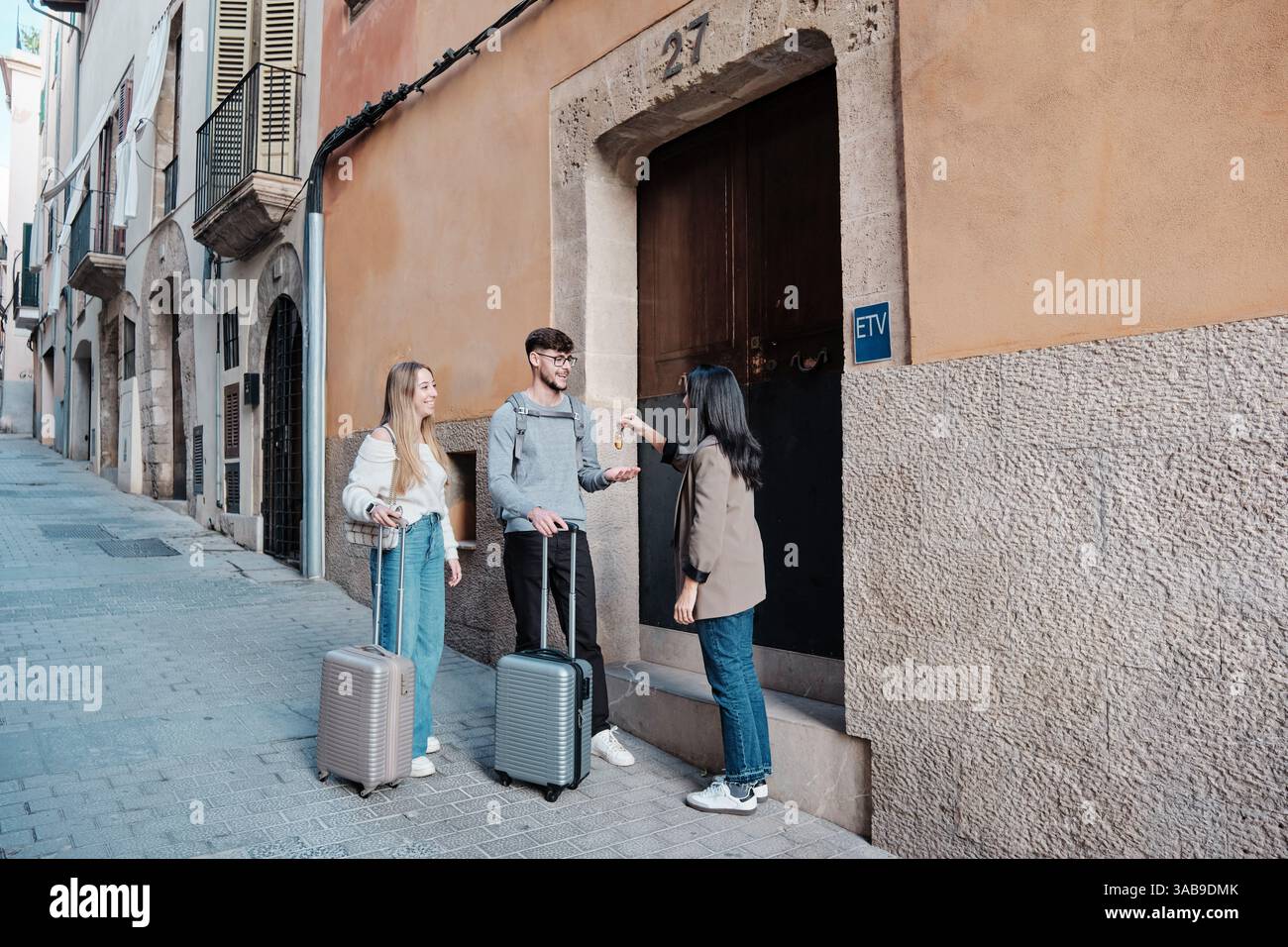 Un jeune couple se tient debout avec des bagages, recevant les clés de leur maison de vacances d'un agent immobilier. Ils sont dans une charmante rue à Majorque, Espagne, e Banque D'Images