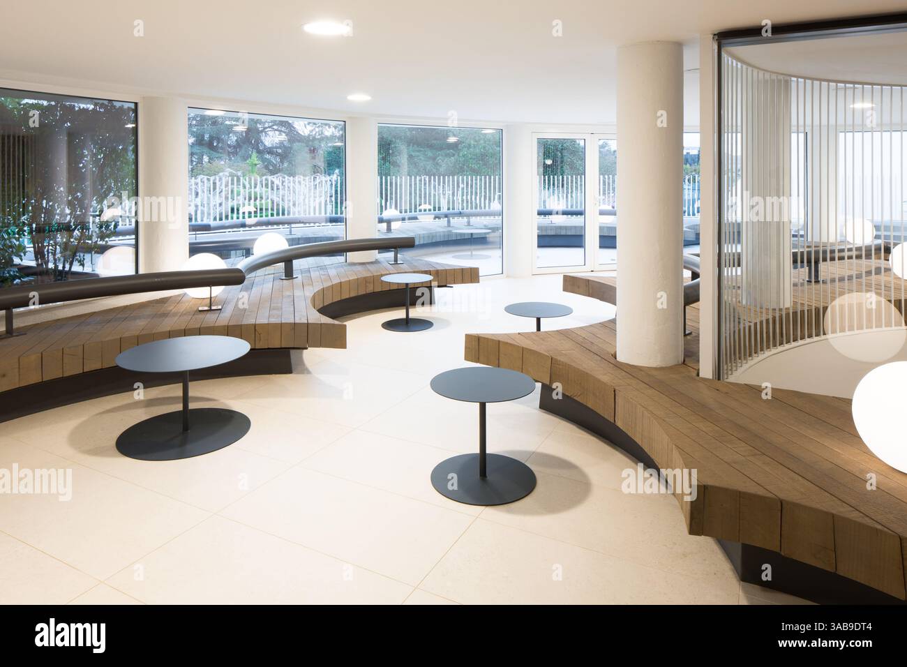 Intérieur club contemporain avec sièges circulaires en bois et élégantes tables noires. Les grandes fenêtres fournissent la lumière naturelle, créant un Mo Banque D'Images